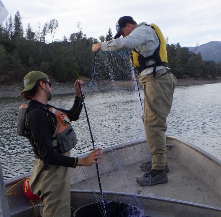 Image shows two men standing in a boat, holding a gill net between them. 