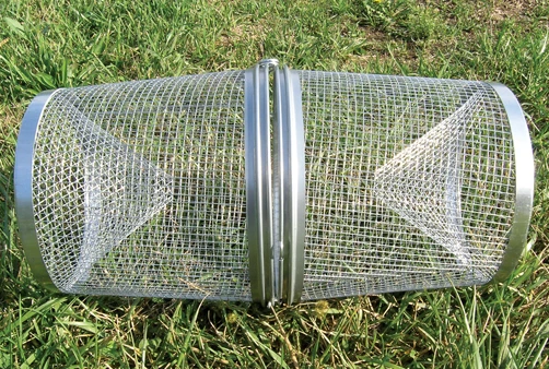 Image shows a metal minnow trap sitting in the grass.